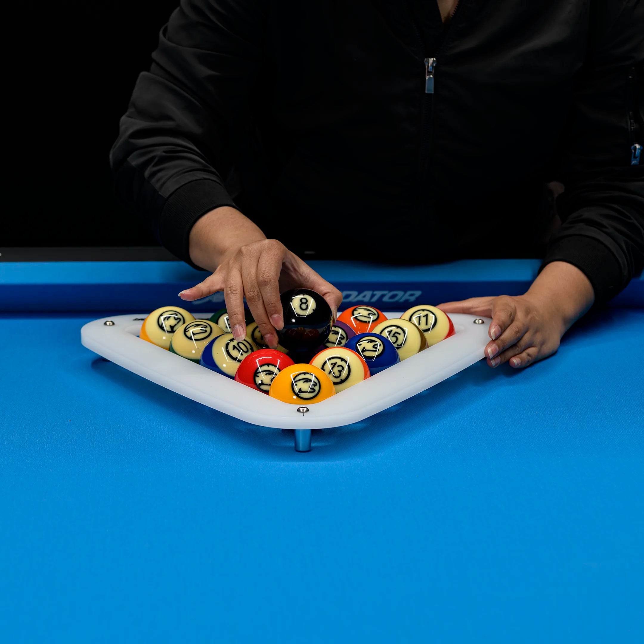 Person arranging pool balls on a white rack with a blue pool table background.