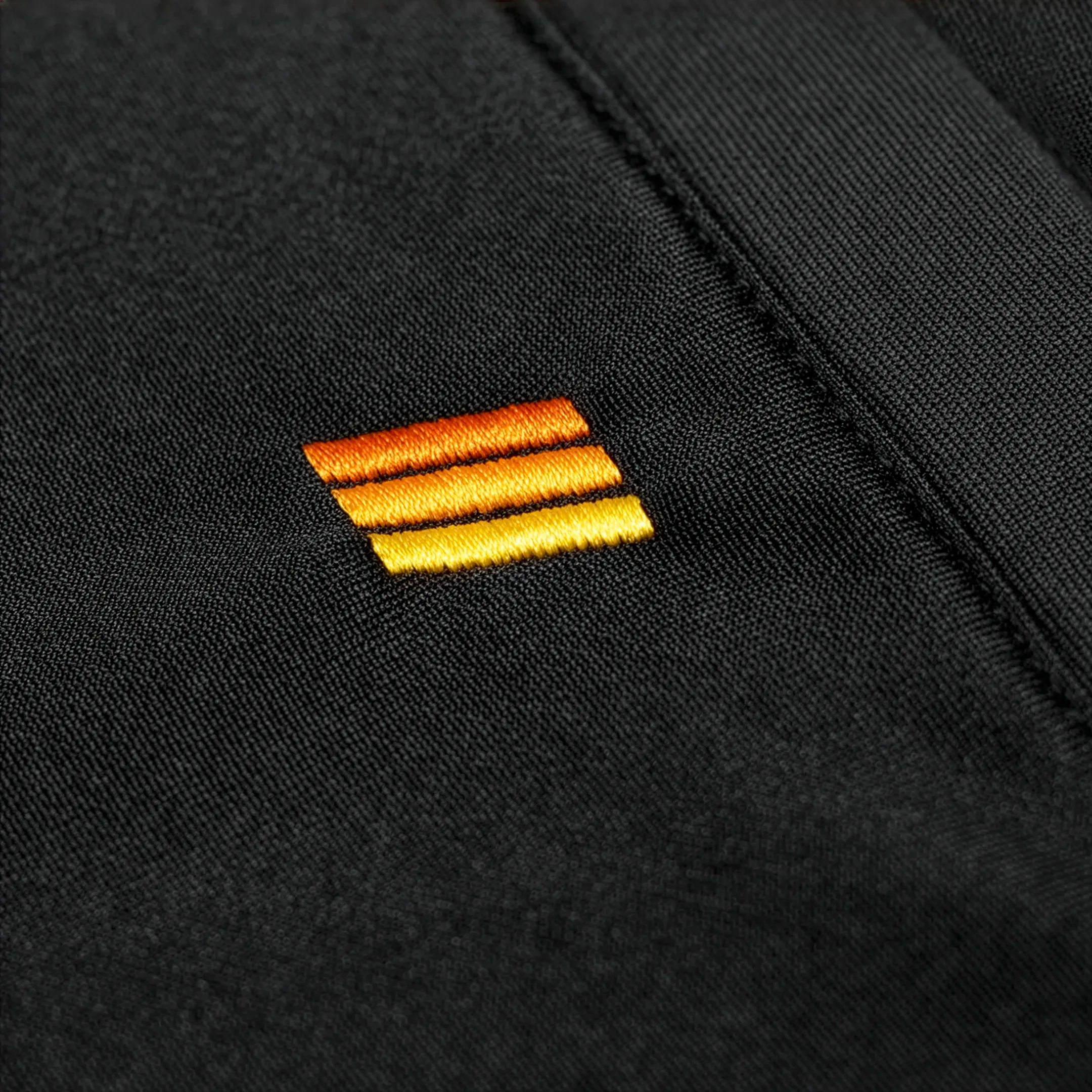 Close-up of a black fabric with a gold and orange embroidered logo.