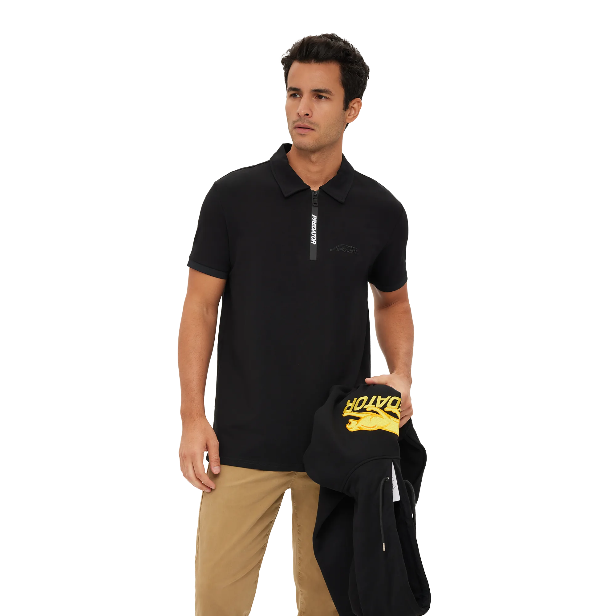 Man wearing a black polo shirt with a zipper and beige pants, holding a black jacket with yellow text.