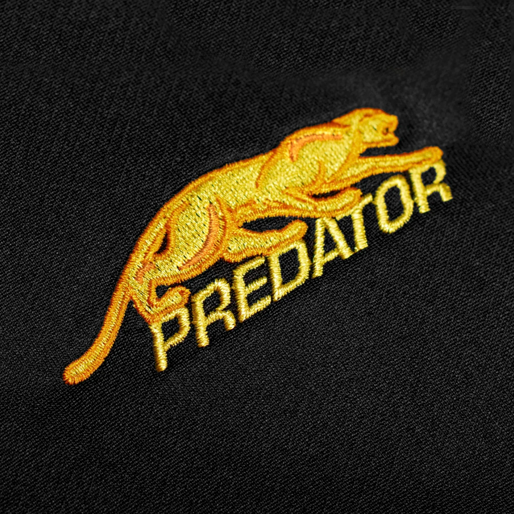 Gold embroidered Predator logo against a black fabric background.
