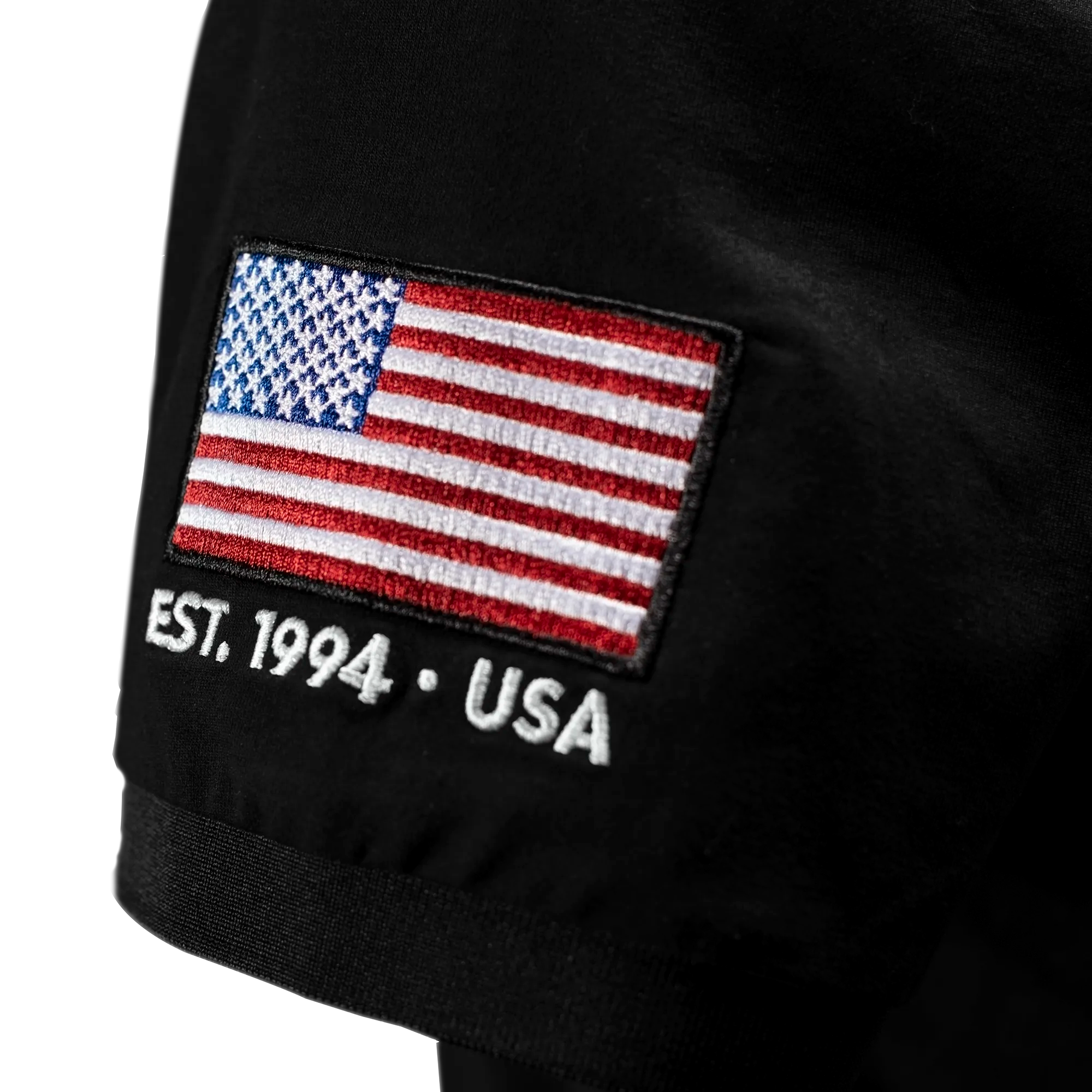 Black polo shirt with American flag patch and 'EST. 1994 • USA' text.