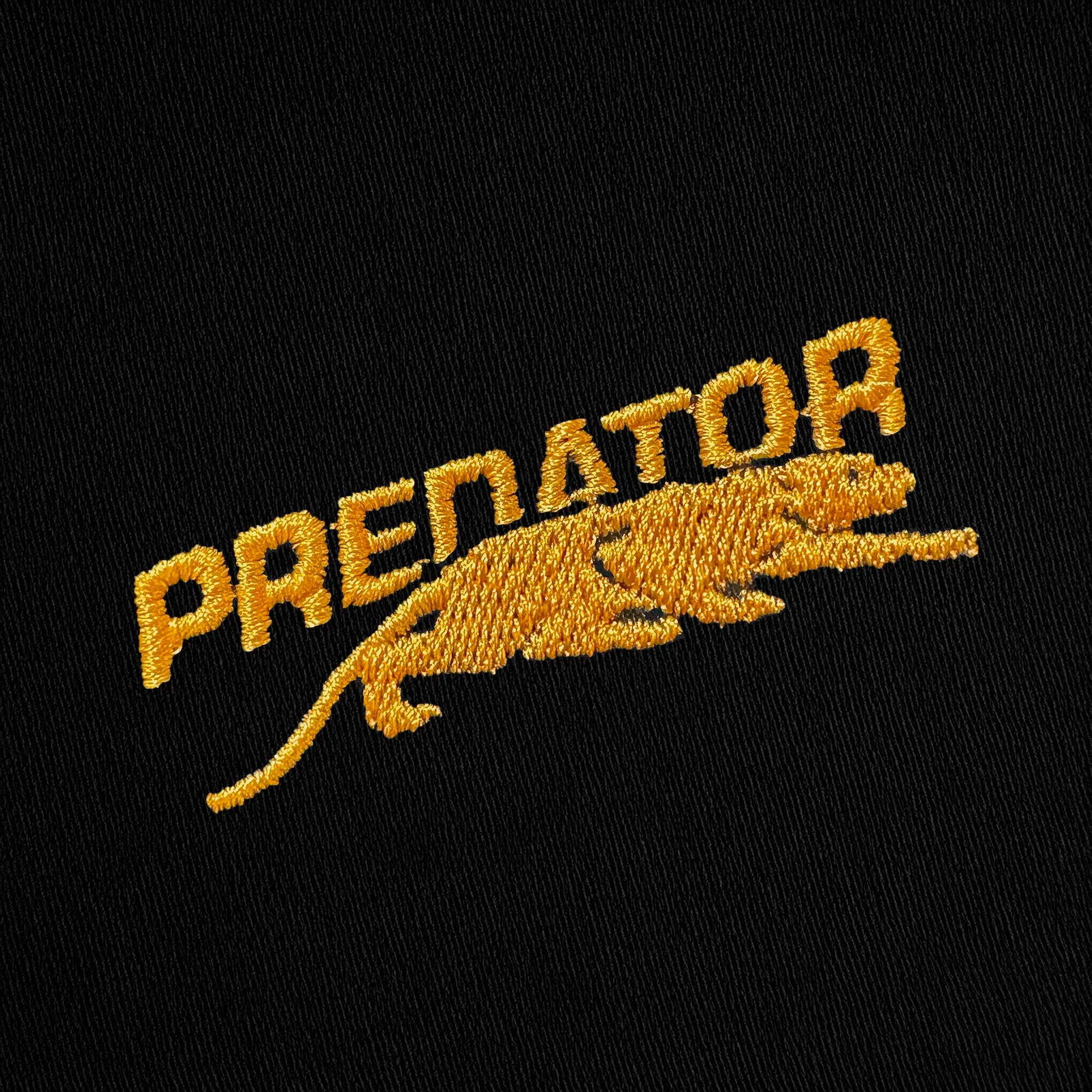 Gold embroidered Predator logo against a black fabric background.