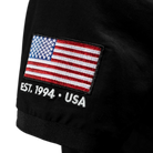 Black polo shirt with American flag patch and 'EST. 1994 • USA' text.