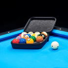 Set of pool balls in a black case on a pool table with a blue surface.