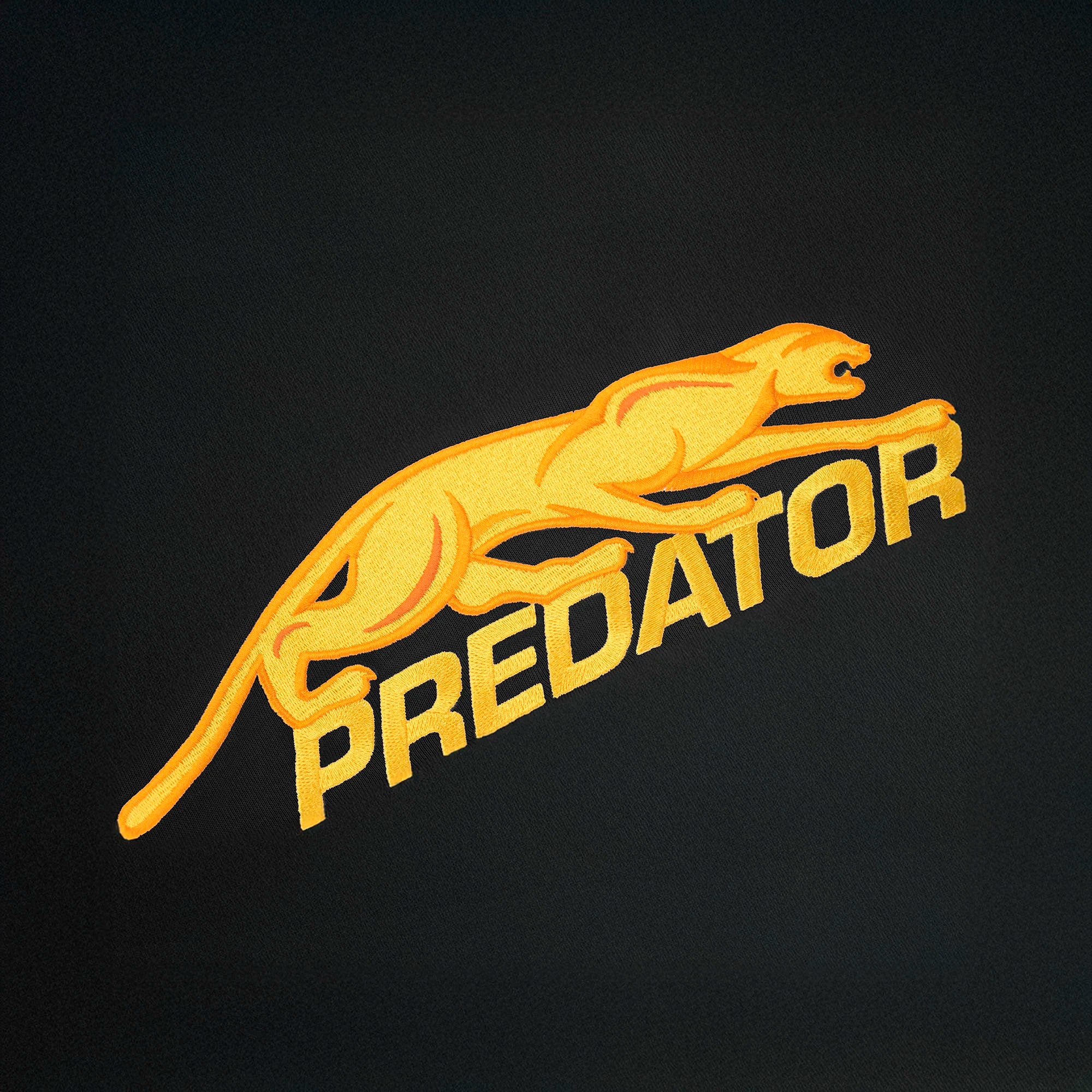 Gold embroidered Predator logo against a black background.