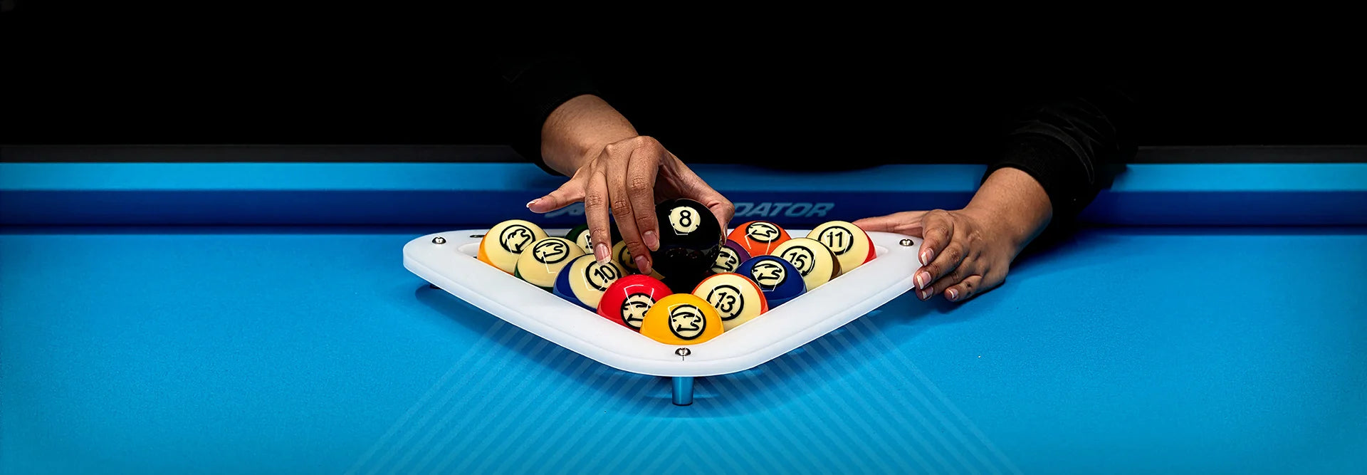 Person arranging pool balls on a white rack with a blue pool table