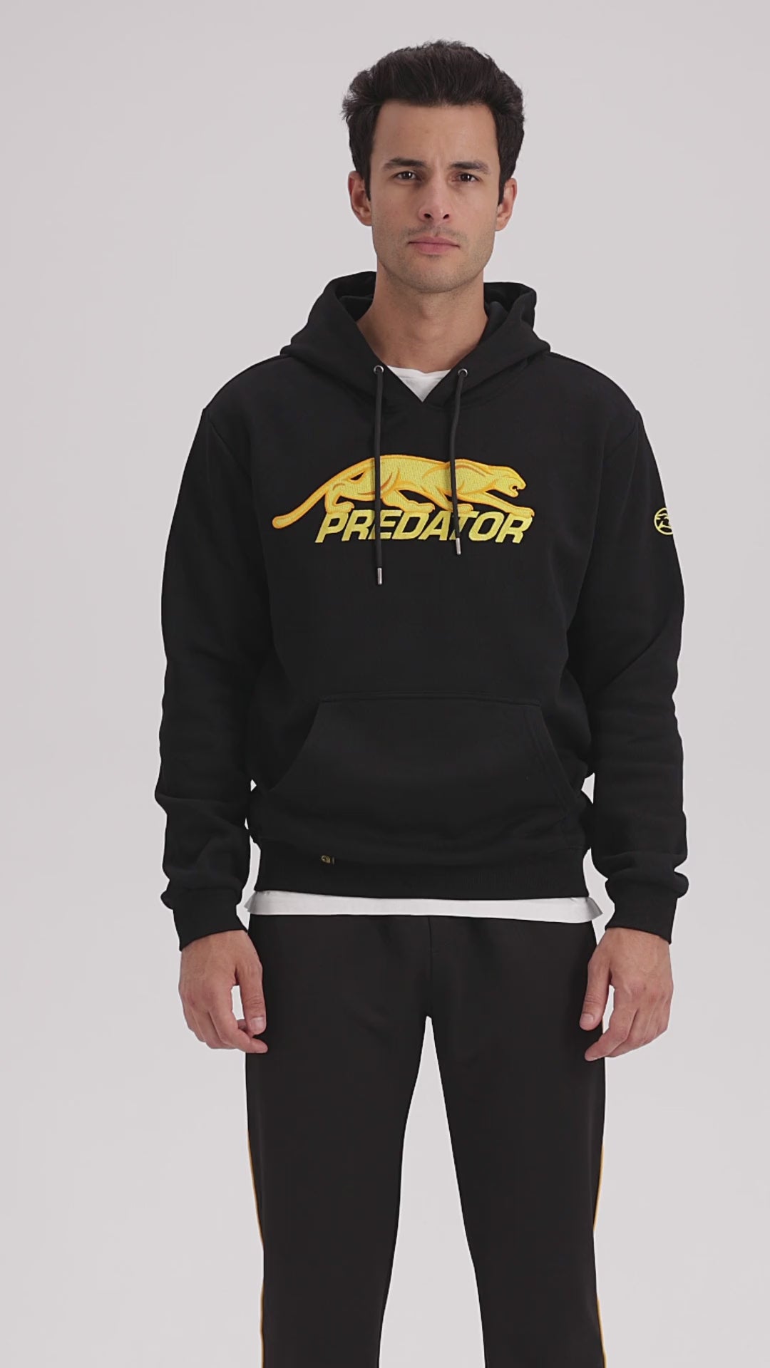 Man with dark hair wearing black hoodie with gold embroidered PREDATOR logo