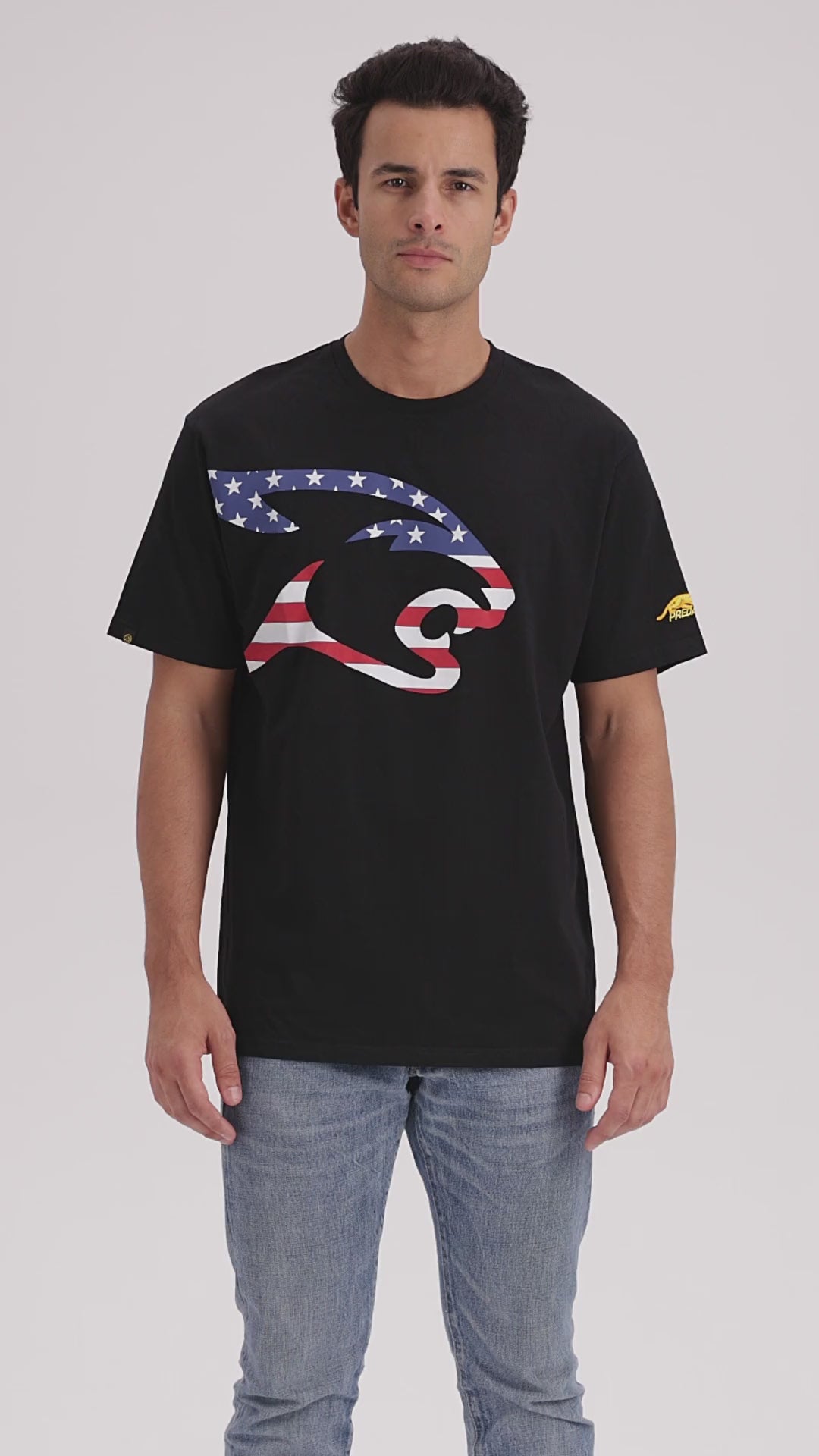 Man with dark hair wearing blue jeans and black t-shirt with United States flag cat head logo